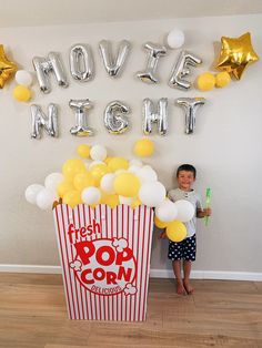 a young boy standing in front of a popcorn box with balloons and streamers around it