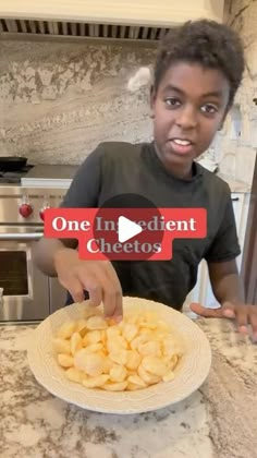 a young boy is pointing at a plate of potato chips on the kitchen counter with one ingredient cheetos sticker in front of him