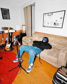 a man sitting on top of a couch in a living room next to a guitar