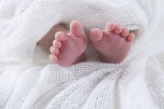 a baby's feet are laying on a white blanket, with pink toes sticking out