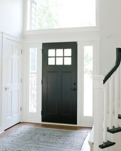 a black door is in the middle of a white room with an area rug on the floor