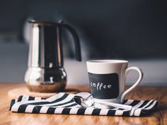 a coffee cup sitting on top of a table next to a tea pot and spoon