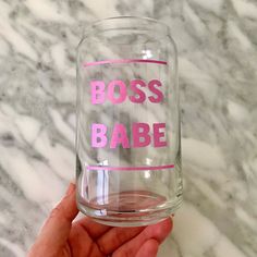 a person holding up a glass with the words boss babe on it in pink lettering