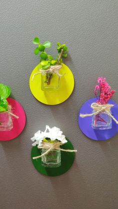 four different colored vases with flowers in them on a gray surface and tied to the wall