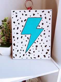 a painting with a blue lightning bolt on it sitting on top of a white shelf next to a potted plant