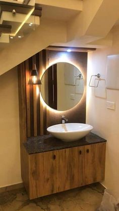 a bathroom sink sitting under a round mirror on top of a wooden cabinet next to a stair case