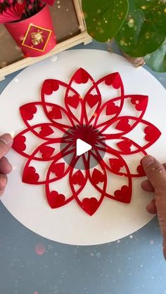 someone is cutting out hearts on a white plate with red paper in the shape of a flower