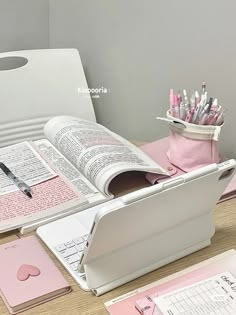 an open book sitting on top of a wooden table next to pens and pencils