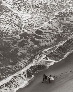 two people walking on the beach with surfboards