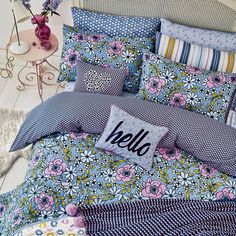 a bed covered in blue and pink flowers with hello written on the pillow case next to it