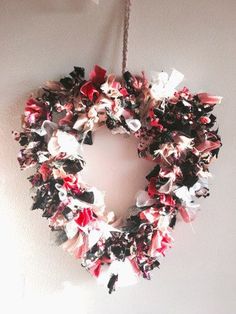 a heart shaped wreath hanging from a rope on the wall with pink and white flowers