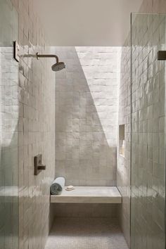 a walk in shower sitting under a window next to a white tiled wall and floor