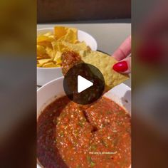 a person holding a tortilla chip over a bowl of salsa