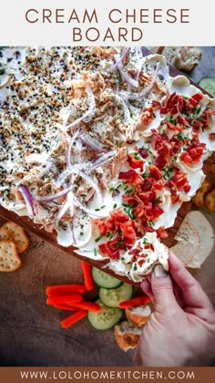 a hand holding a cracker with cheese and vegetables on it next to crackers