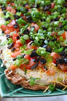 an enchilada dish is on a green platter with cheese and black olives