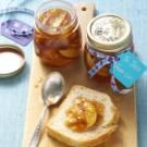 a wooden cutting board topped with jam and bread next to a jar of peanut butter