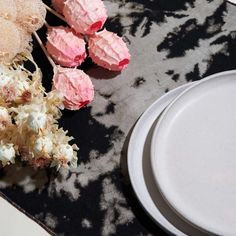 some pink flowers are next to a plate with cake on it and another white plate