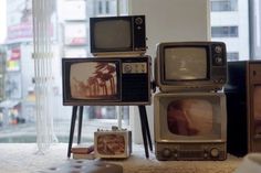 an assortment of old televisions sitting on top of a rug in front of a window