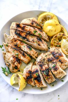 grilled chicken with lemons and herbs on a white plate