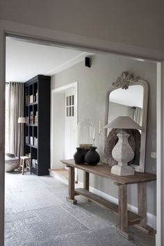 a table with vases on it in front of a mirror and bookshelf