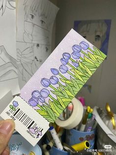 a person holding up a ticket with flowers on it in front of some art supplies