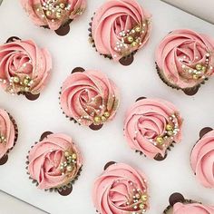 cupcakes with pink frosting and gold decorations are arranged on a white tray