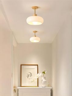 a hallway with white walls and wood flooring is lit by three lights above the fireplace