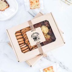 a box filled with cookies sitting on top of a white marble counter next to slices of cake