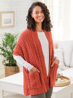 a woman standing in front of a couch wearing an orange cardigan