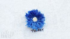 a small blue flower with the word turkey on it's side, sitting on a piece of white fabric