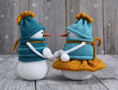 two knitted snowmen sitting next to each other on top of a wooden table