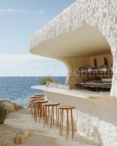 an outdoor bar next to the ocean with lots of stools and bottles on it