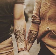 two people are holding hands with tattoos on their arms and one has a wolf tattoo on his arm