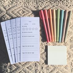 several different colored pencils next to each other on a blanket with writing paper and pen