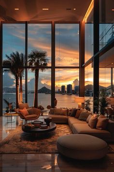 a living room filled with lots of furniture and large windows overlooking the water at sunset