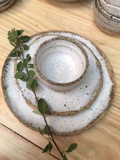 three white plates with green leaves on them sitting on a wooden table next to other dishes