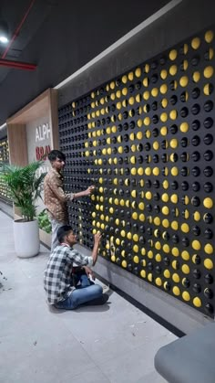 two men sitting on the ground next to a wall with yellow and black circles painted on it