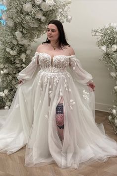 a woman wearing a white dress with flowers on it and thigh high heels standing in front of a floral arch