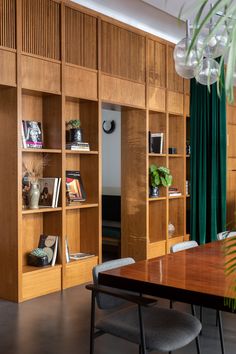 a dining room table and chairs in front of wooden bookshelves with green curtains