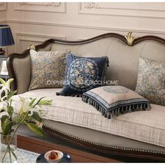 a couch with many pillows on it and a vase full of flowers in the corner