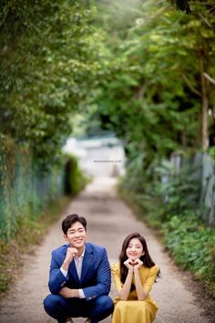 two people sitting on the ground next to each other in front of trees and bushes