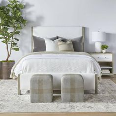 a bedroom with white and gray furniture and pillows on the bed, along with a potted plant