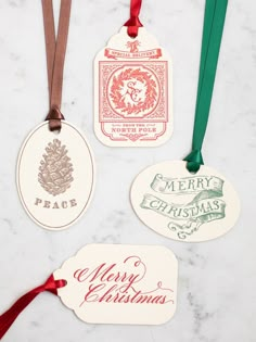 three christmas tags with ribbons hanging from them on a marble countertop in front of a red ribbon