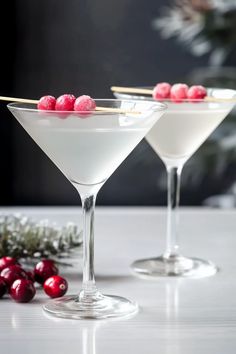 two martini glasses filled with white wine and cranberry garnish on a table