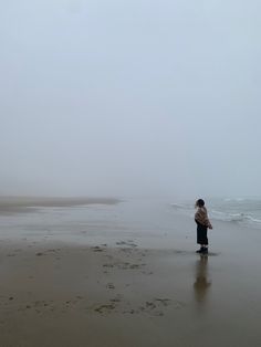 a man standing on top of a sandy beach next to the ocean under a cloudy sky