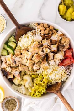 a white bowl filled with chicken salad next to lemons and seasoning on the side