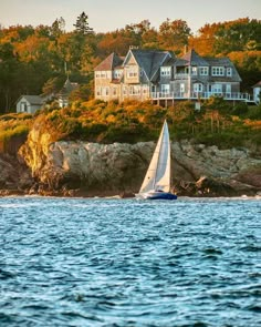 a sailboat is in the water near a large house on a cliff overlooking the ocean