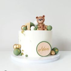 a teddy bear sitting in the top of a cake with gold and green decorations on it