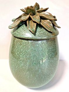 a green ceramic jar with a flower on the top and leaves sticking out of it