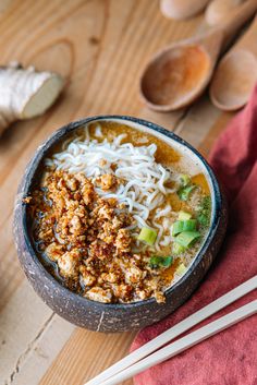 a bowl filled with noodles and meat next to chopsticks on a wooden table